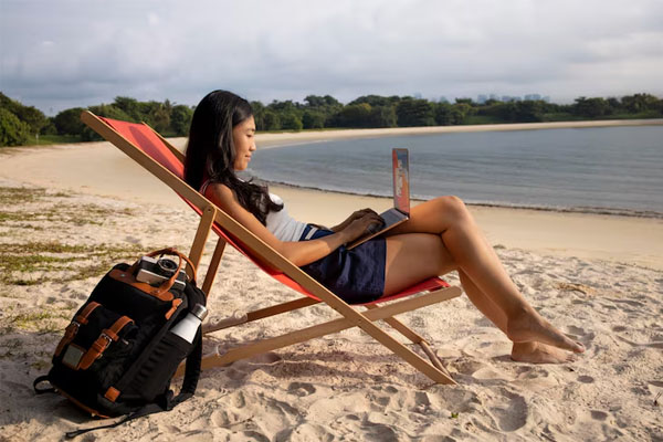 ragazza in sedia a sdraio digitando sul portatile sulla spiaggia