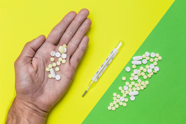 una mano che tiene alcune pillole accanto a un termometro e pillole su uno sfondo verde e giallo