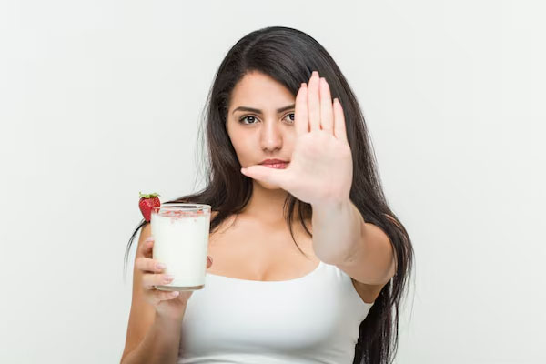 Donna che fa il segnale di stop con una mano e tiene un bicchiere di latte con l'altra