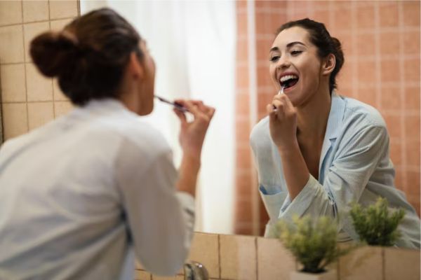 Persona cepillándose los dientes en el baño, mostrando una sonrisa saludable